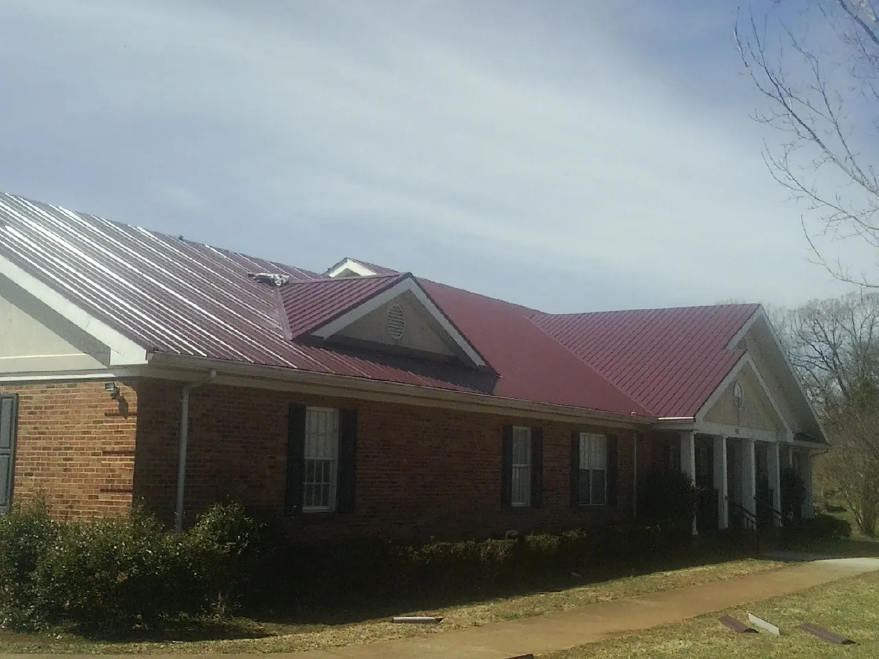 Red metal roof with gabled entries on a long brick building, from a Hail Damage Roof Repair job in Montpelier Station