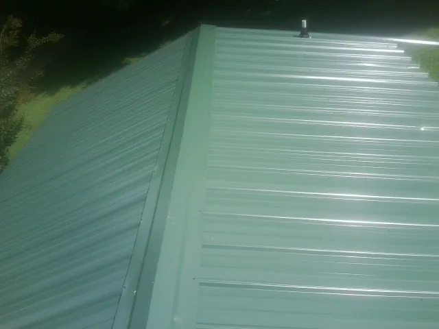 New green metal panels meeting at the ridge of a roof — Flat Roof Repair work by our crew in Montpelier Station