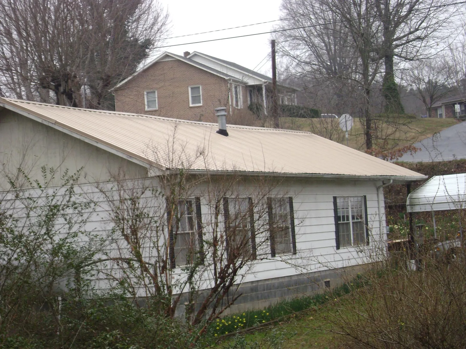 Tan metal roof on a white sided house set into a hillside — Commercial Roofing by Roofing Brothers in Montpelier Station